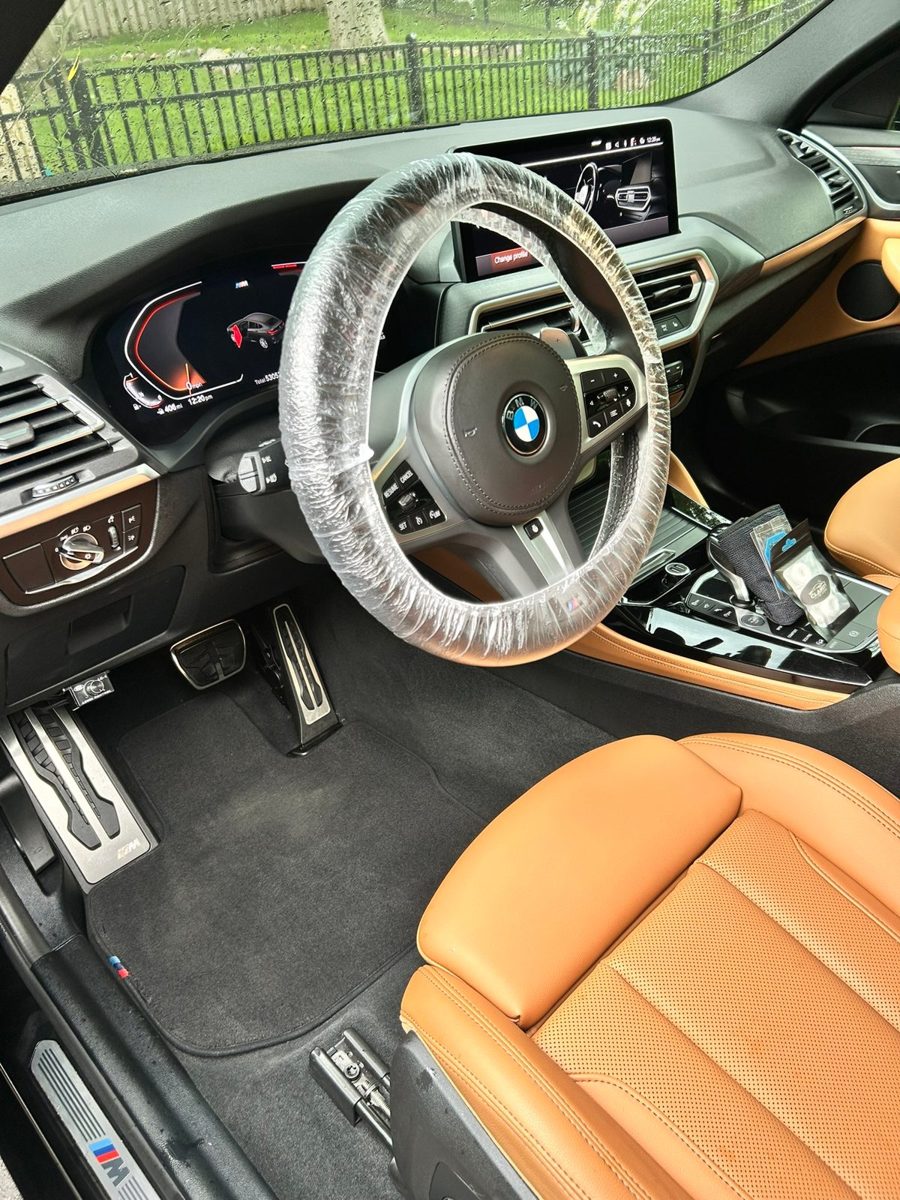 BMW M Sport interior with tan leather seats and clean carpets after an interior detail, with the steering wheel covered