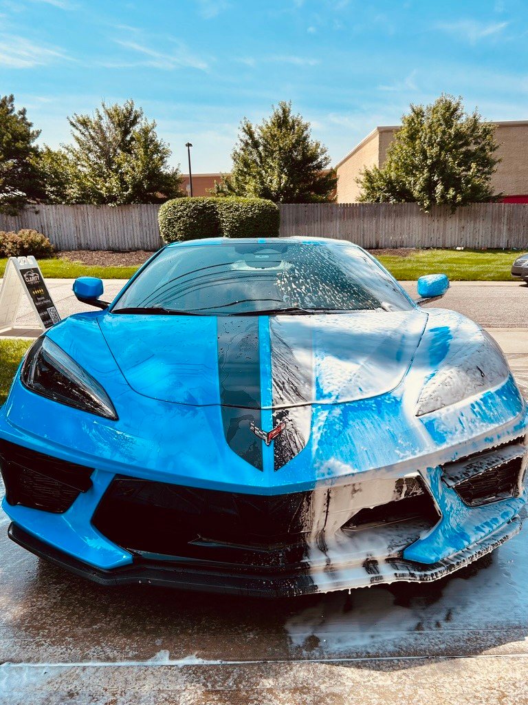 Foam on the front of a blue Corvette during a wash