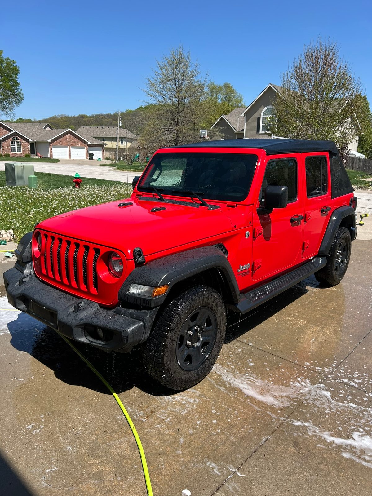 Red Jeep Wrangler being rinsed during a two bucket hand wash in a driveway