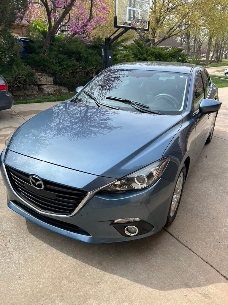 Blue Mazda3 with a blossoming tree reflected in the hood after a detail