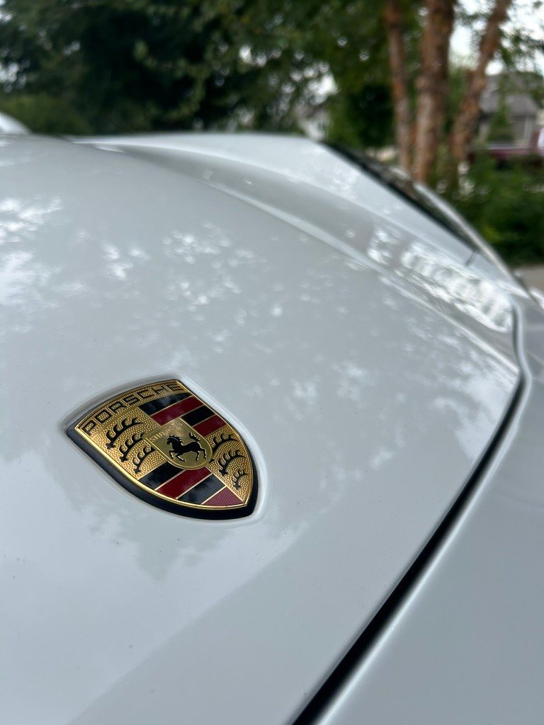 Porsche badge on a freshly cleaned white hood